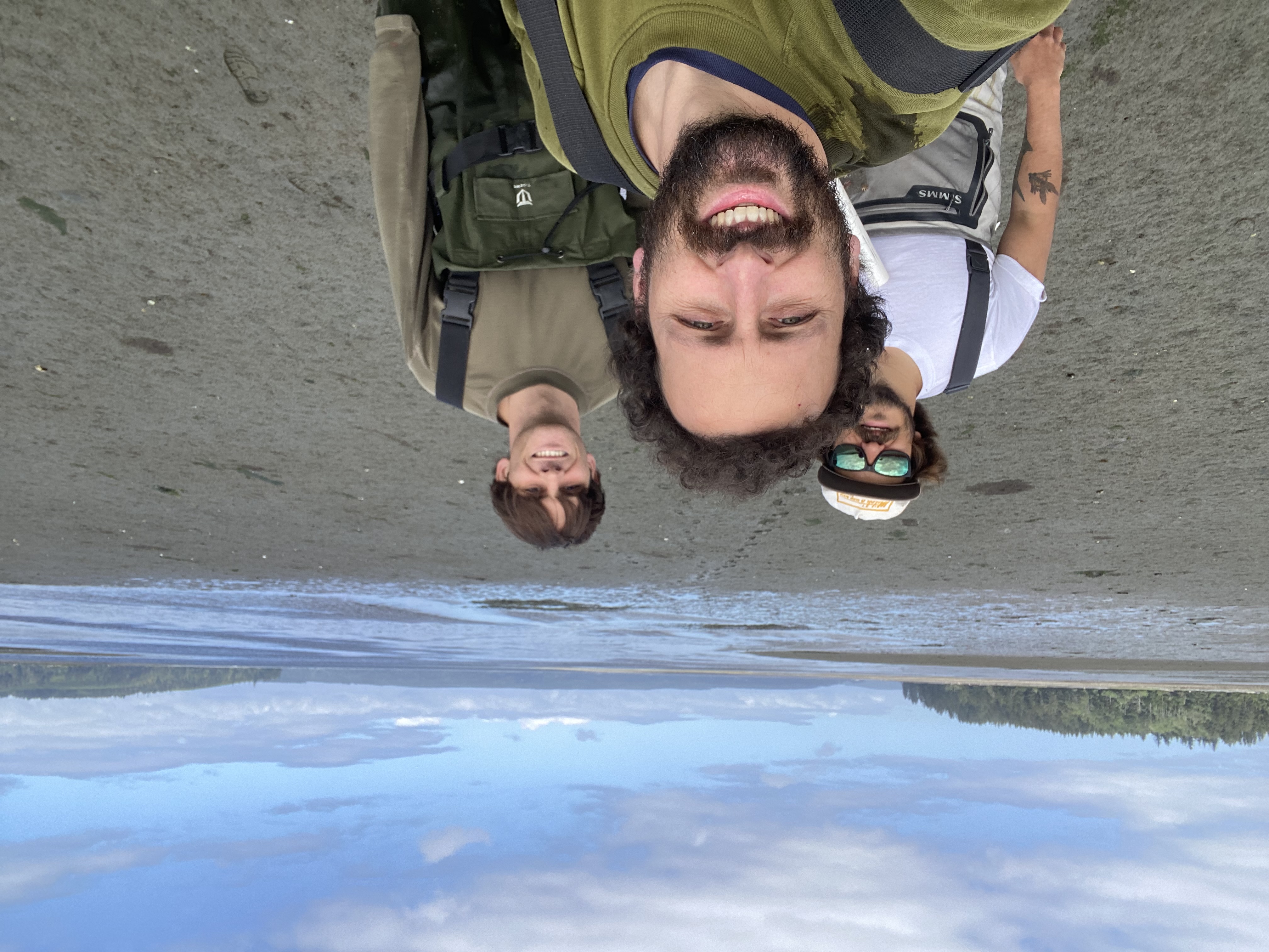 Three field researchers in waders at a coastal estuary.